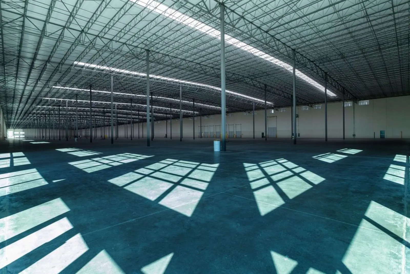 Interior de nave industrial vacía con sombras geométricas de la luz natural sobre el piso